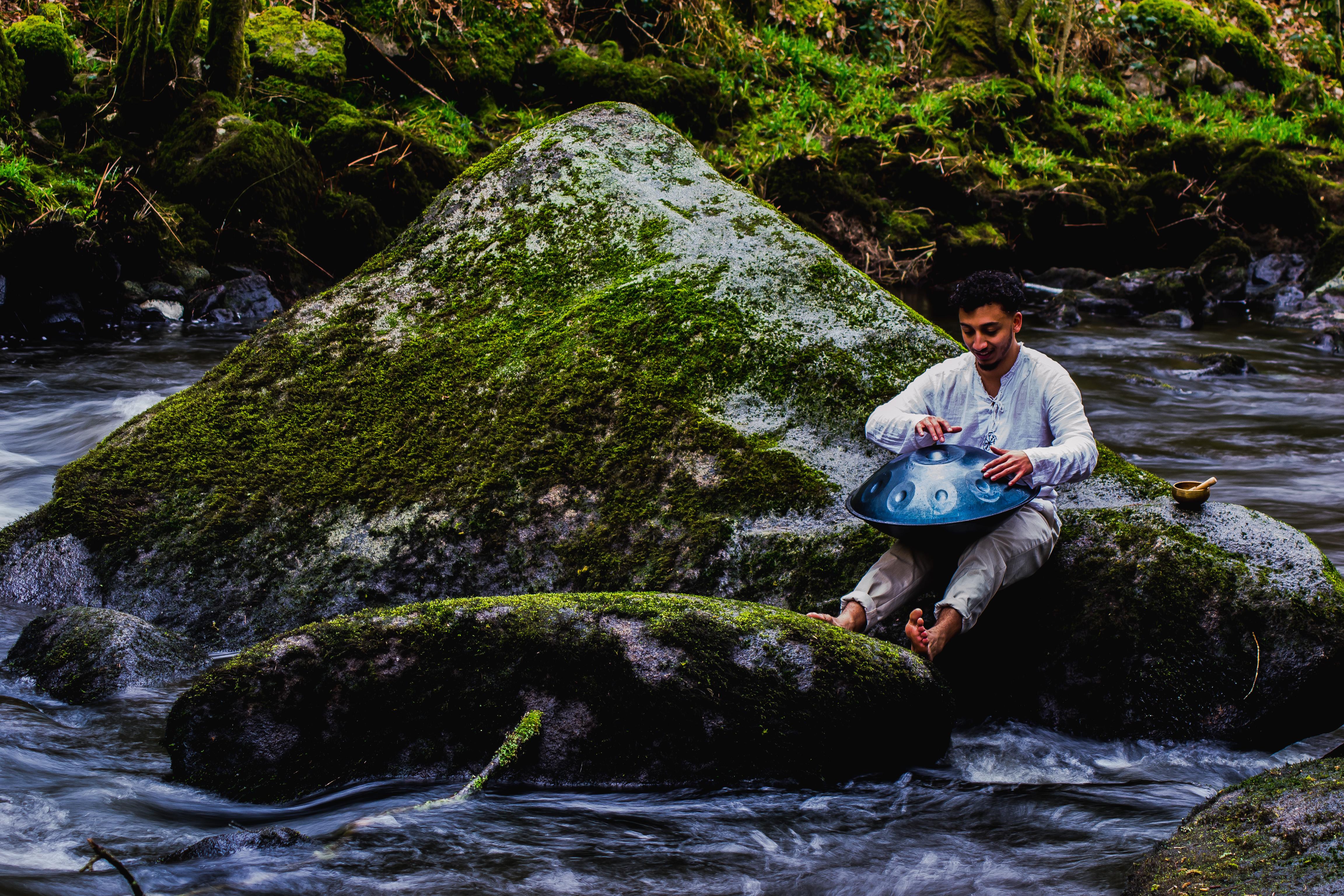 Joran jouant du hang drum sur un rocher au milieu de la rivière