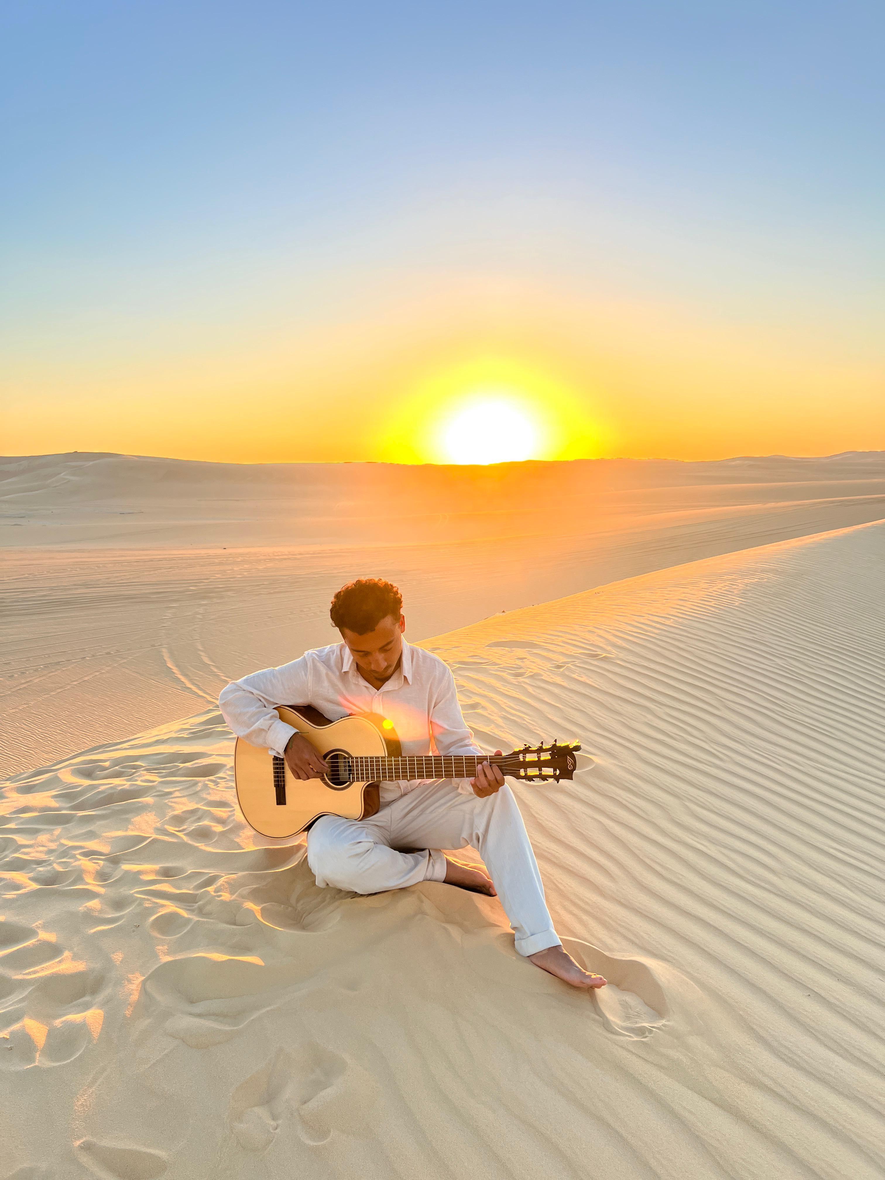 Joran Ferragu jouant de la guitare dans le désert au coucher du soleil